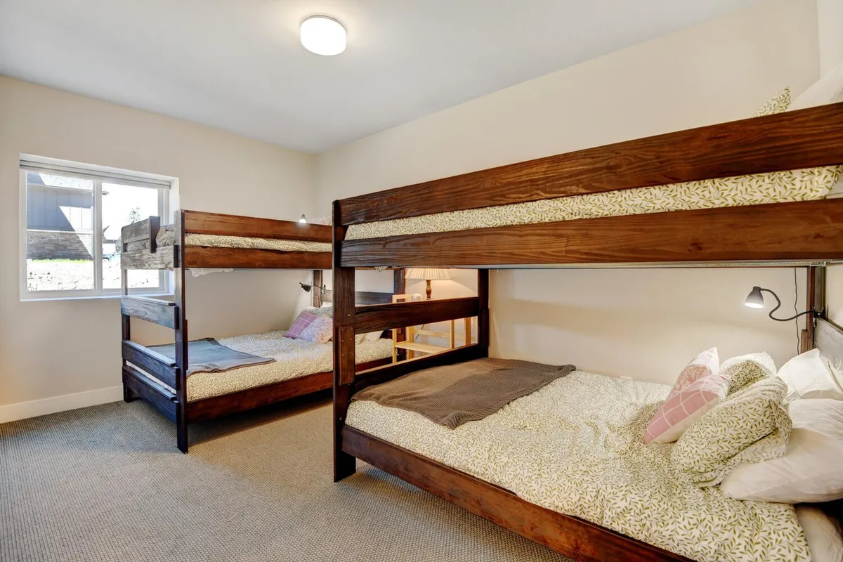 A cheerful bunk room with sturdy bunk beds dressed with decorative pillows, a nearby window streaming in natural light, and playful touches. The space is designed for both sleeping and relaxing, inviting group and family stays.