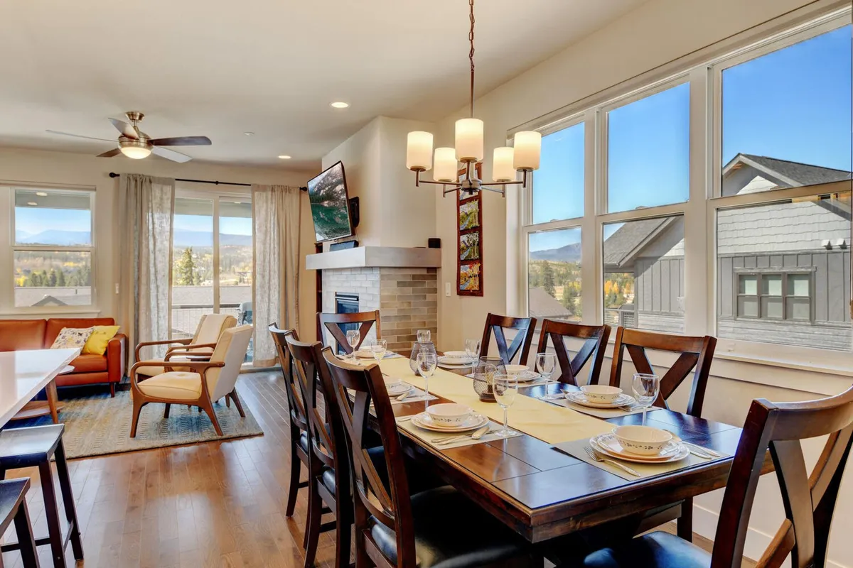 A warmly lit open-concept living and dining area, featuring a dining table set for a meal, a comfortable couch, and a fireplace with a TV mounted above. The space exudes coziness and is clearly designed for gatherings, relaxation, and memorable family or group experiences.