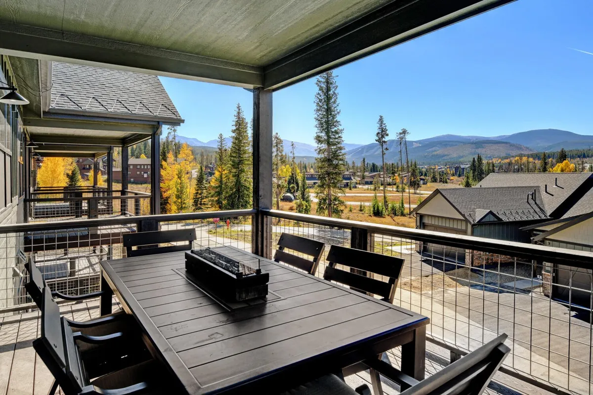 An outdoor dining table set on a deck with expansive mountain views and surrounding trees. The table is ready for gatherings and is bathed in natural light, inviting guests to dine and socialize while immersed in nature.
