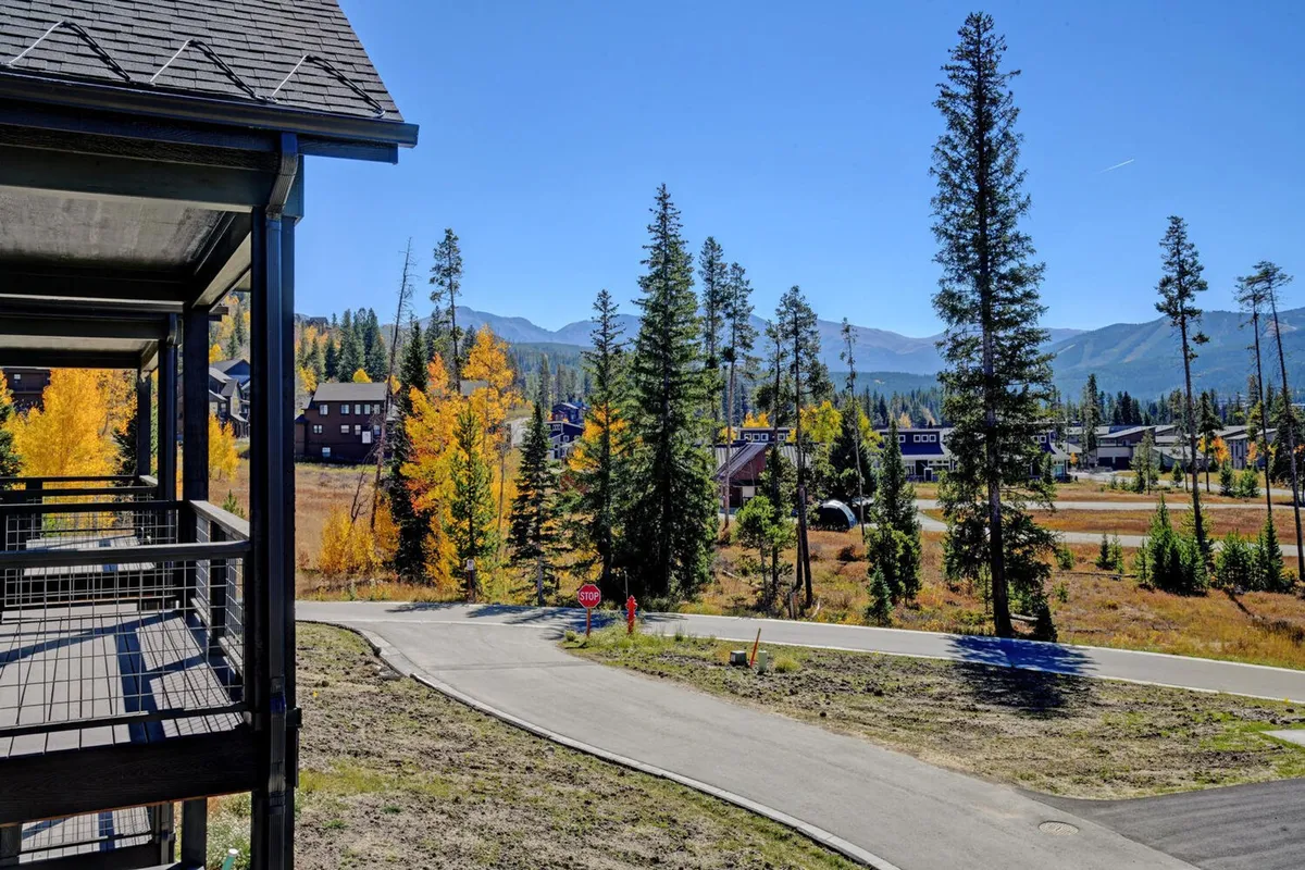 An exterior landscape capturing golden autumn trees, snow-capped mountains in the distance, a winding road, and cozy cabins, suggesting immediate access to nature trails and scenic views.