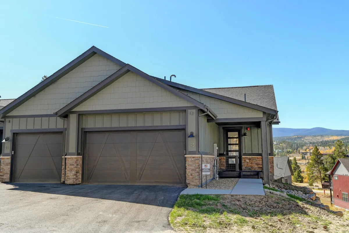 The exterior of the home features a spacious entryway with large garage doors and attractive landscaping. The garage area is clearly visible, hinting at the ample storage space for outdoor gear like skis and bikes, while the entry area feels welcoming and functional.