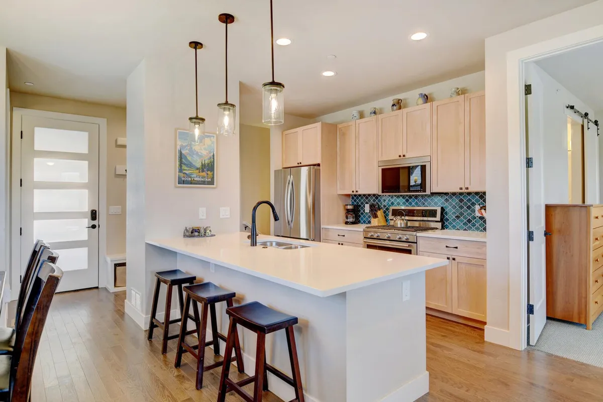 A modern kitchen with a spacious island countertop, bar stools for casual seating, and state-of-the-art appliances. The area is styled for both cooking and socializing, featuring tasteful wall art and a cozy, inviting mood.