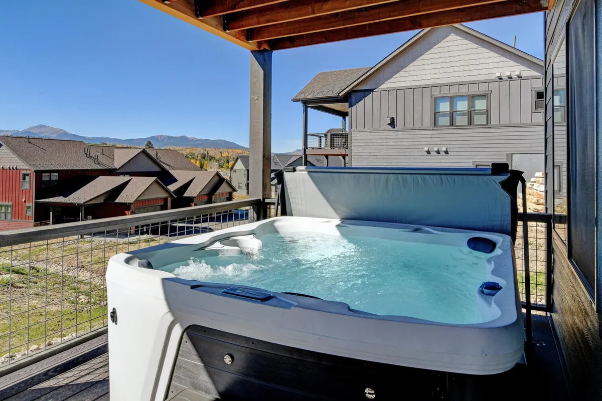 An inviting outdoor hot tub on a deck overlooking a panoramic mountain view, with a tranquil sunset sky and comfortable seating. The setting exudes relaxation after a day of adventure.