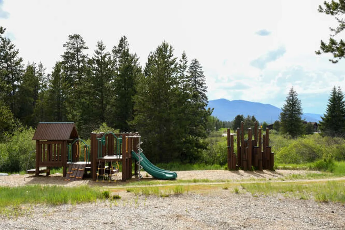An exterior view of a community playground surrounded by trees, with slides and play structures. The area is filled with energy, suggesting a family-friendly community and opportunities for outdoor fun for children.