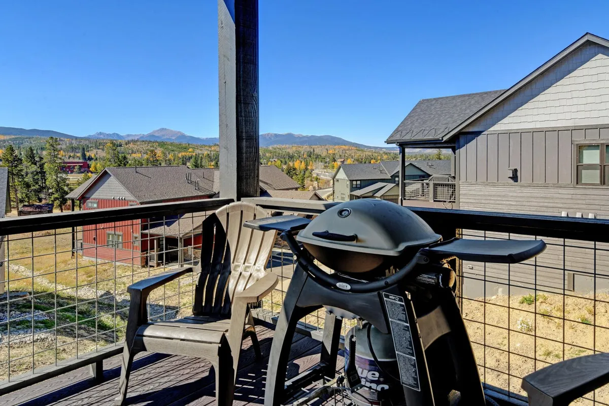 A cozy deck featuring a BBQ grill and comfortable chairs, perfectly positioned to enjoy panoramic mountain views. The scene is set for an evening gathering, with the grill ready for outdoor feasts and the natural backdrop enhancing the mountain living experience.