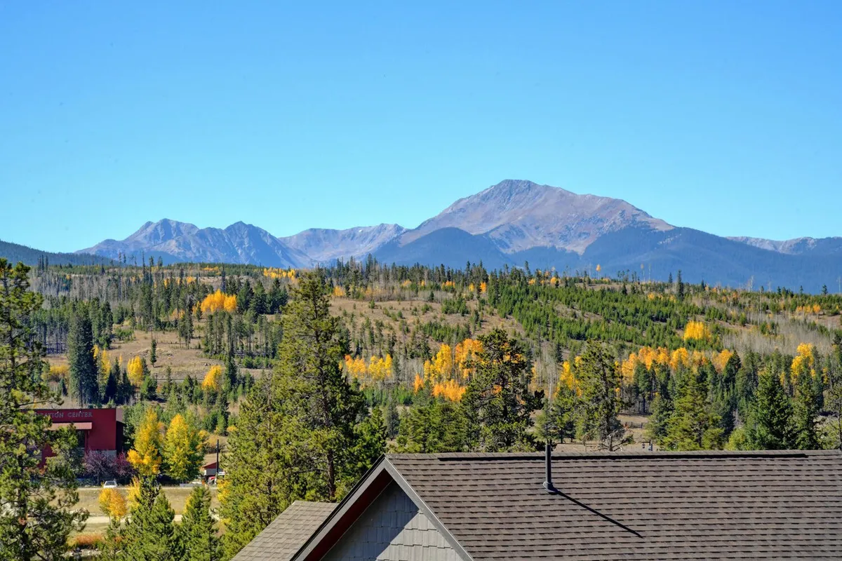 A panoramic view of a mountain range with dense forest and colorful foliage, with the rooftop of a house peeking into the frame. The peaceful setting evokes the natural beauty surrounding the chalet, with opportunities for hiking, photography, and relaxation.