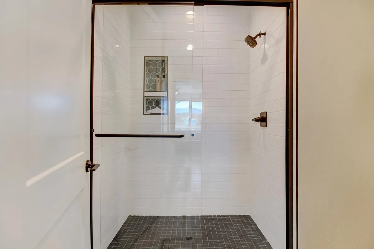 A modern bathroom featuring a glass shower enclosure, hexagonal niche for toiletries, and dark tiled floor. The space feels inviting and spa-like, with thoughtful design elements and luxurious bath products visible.